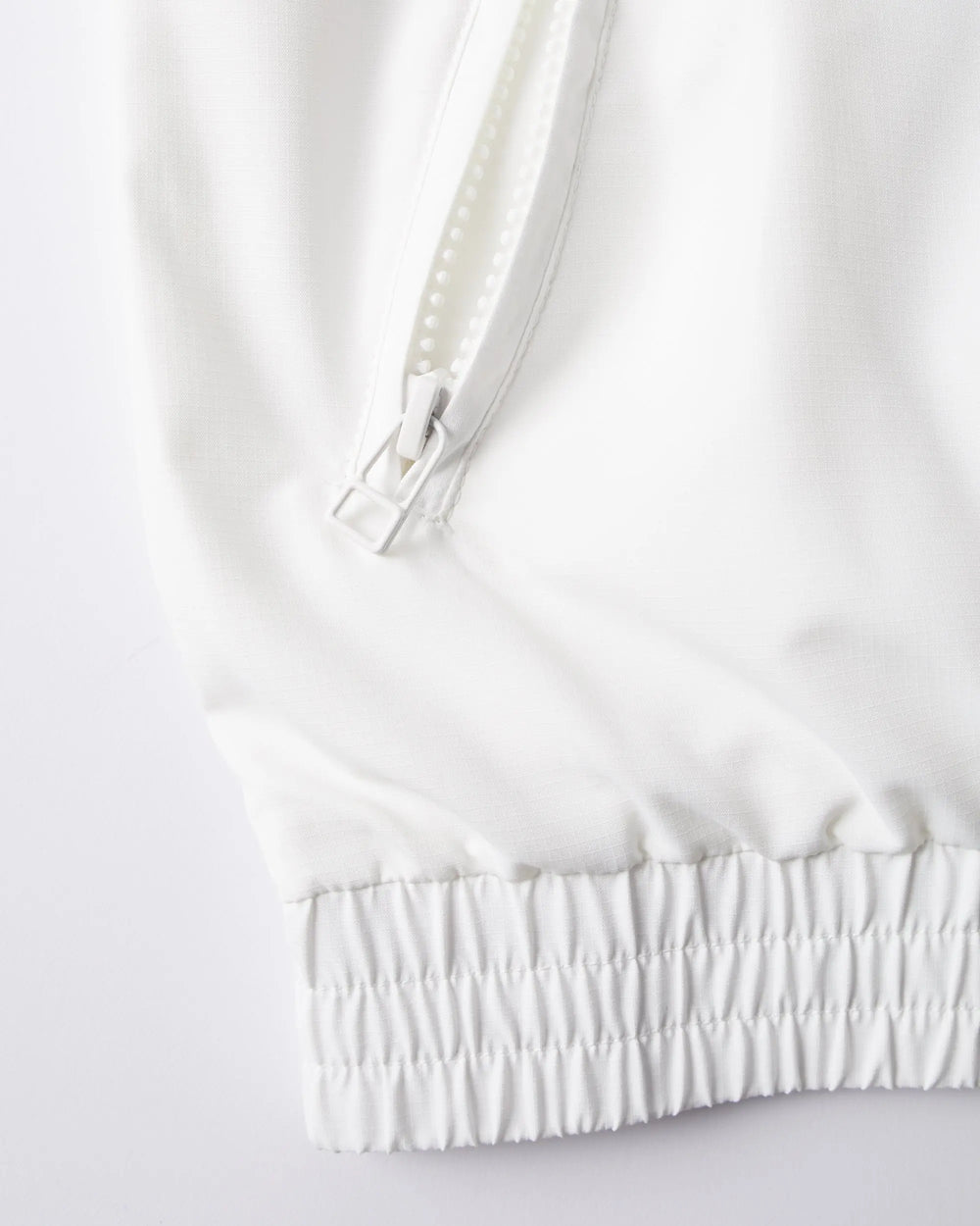 Detail of the white byParra Tennis Maybe? Track Jacket featuring a zippered pocket and elasticated hem.